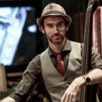 Joe wearing black shirt, tie, hat, holding double bass