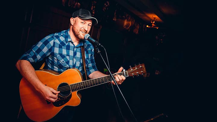 Phil Doughty playing a Martin guitar wearing a blue checkered shirt