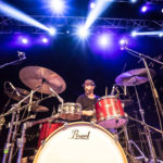 Sam Jones playing drums behind a n extra large drum kit